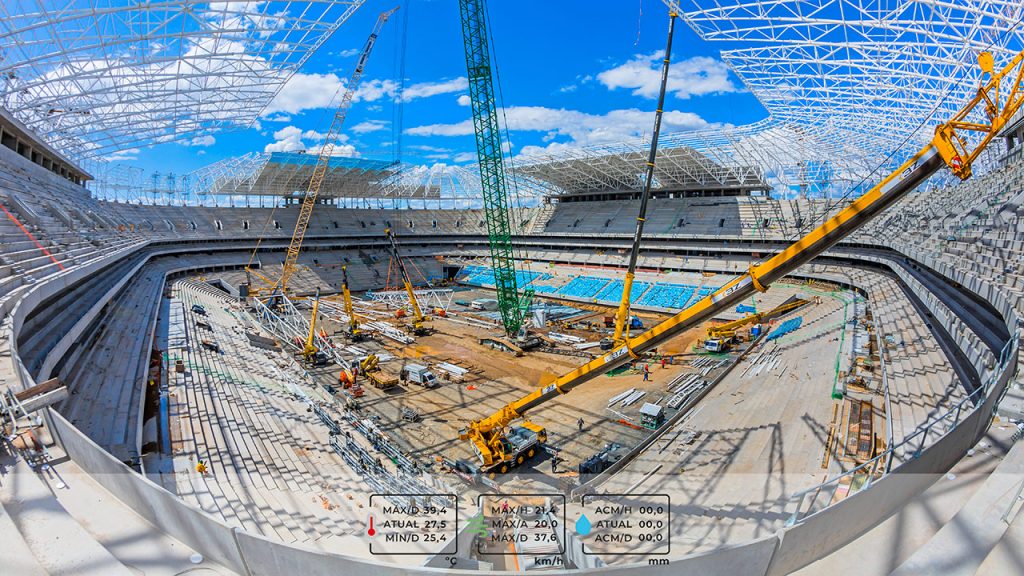 Fotografia fish-eye de obra em estádio com guindastes e estruturas.